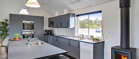 A modern kitchen with a central island, built-in appliances, and a wood-burning stove.