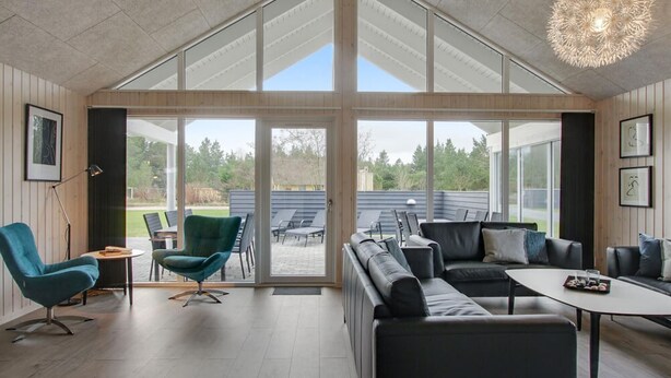 En rummelig opholdsstue med en stor skydedør, der fører til en udendørs terrasse, et behageligt sofasæt og et spisebord.
