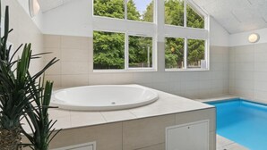 Een moderne badkamer met een vrijstaand bad, een klein zwembad en grote ramen met uitzicht op groen.