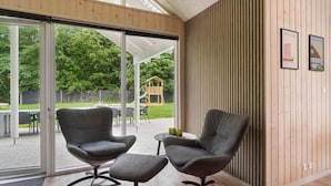 Een moderne kamer met twee grijze fauteuils, een klein tafeltje en een houten wand met ingelijste foto's.