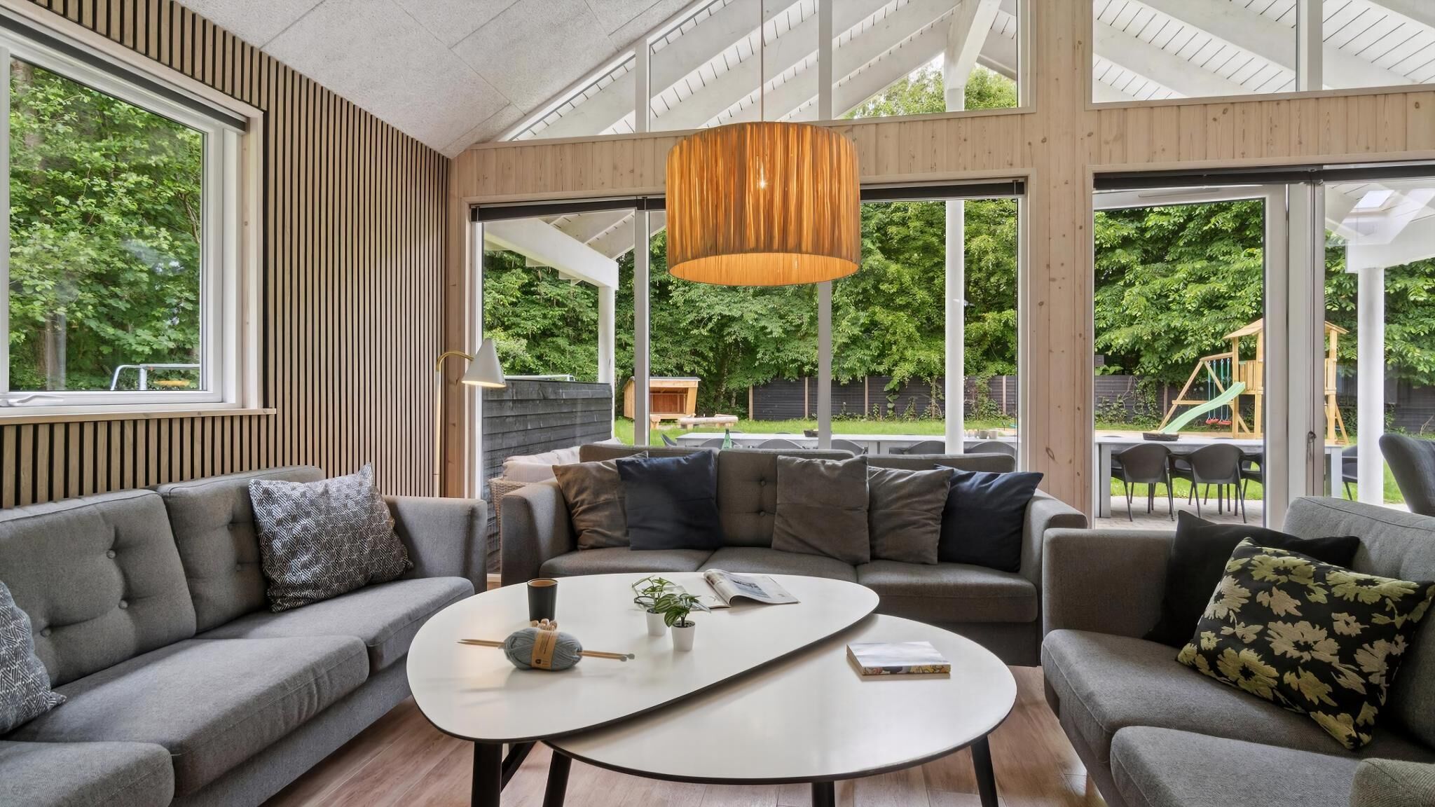 A modern living room with a large window, a wooden ceiling, and a central coffee table.