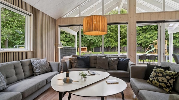 A modern living room with a large window, a wooden ceiling, and a central coffee table.