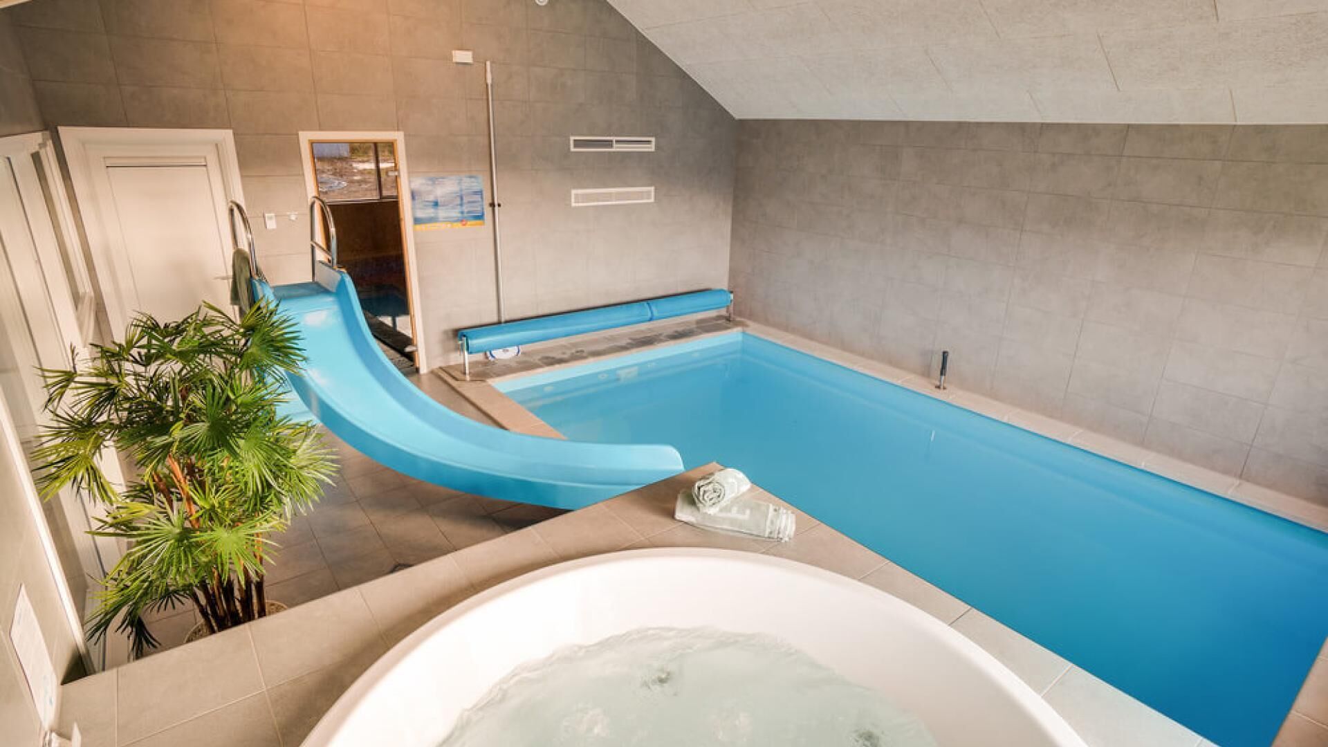 Een modern binnenzwembad met een glijbaan, een jacuzzi en een bank.