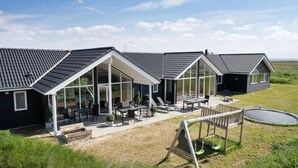 Una casa moderna con amplios ventanales, un patio con mobiliario exterior y una piscina pequeña.