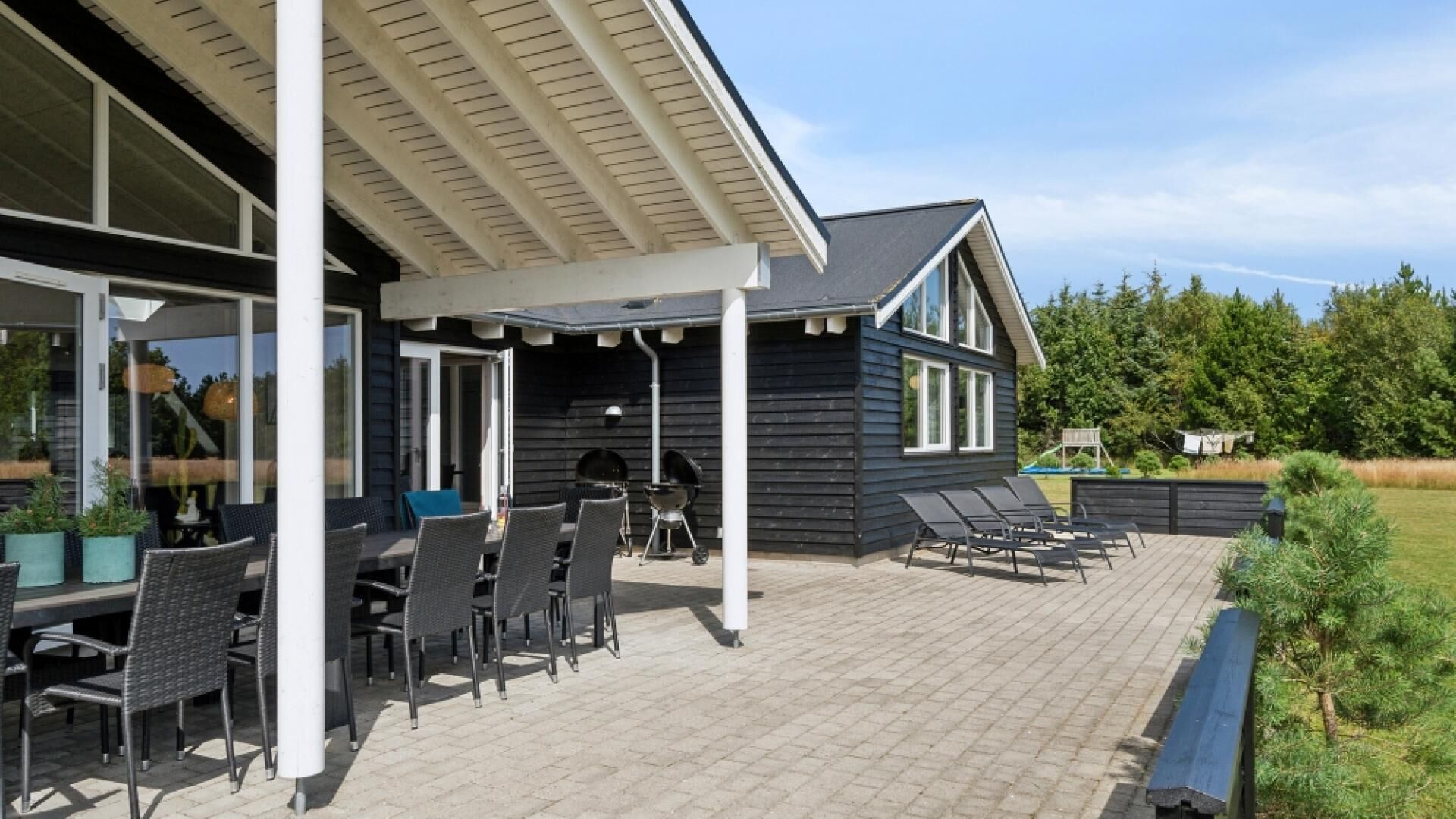 Eine überdachte Terrasse mit Gartenmöbeln, einem Grill und einem Holzdeck.