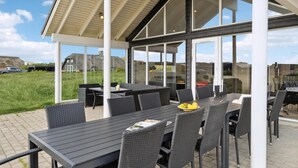 Een terras buiten met tafels en stoelen, grote ramen en uitzicht op het omliggende landschap.