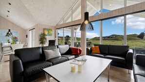 Een modern interieur met een zwarte leren bank, een witte tafel en grote ramen met uitzicht op het omliggende landschap.