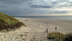 Een strand met duinen, een houten omheining en iemand die loopt.