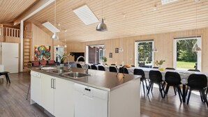 A spacious kitchen with a central island, a dining area with a long table, and large windows offering a view of the outdoors. - VillaVilla 261 - Ho ved Blåvand, Vestjylland (Blåvand)