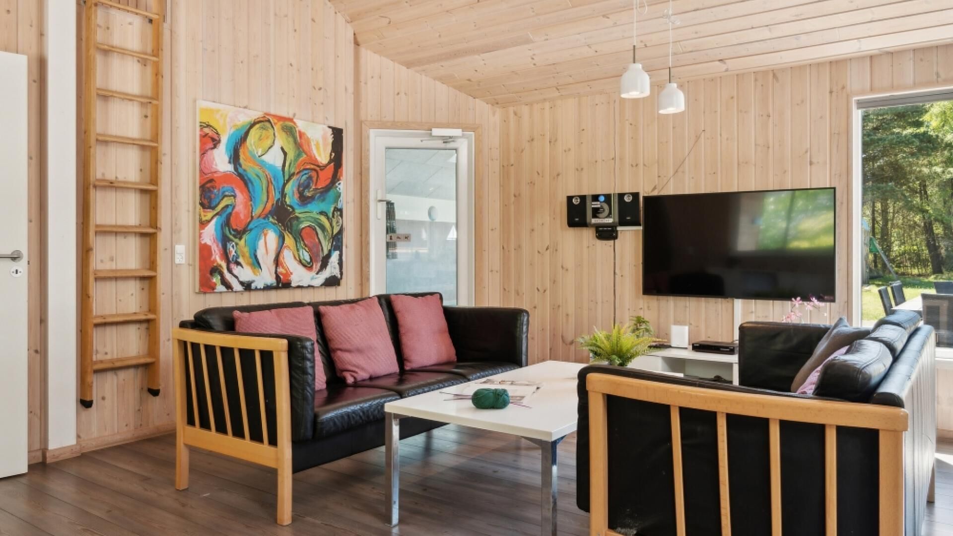 Een gezellige woonkamer met houten inrichting, een zwarte leren bank, een bijzettafeltje en een kleurrijk abstract schilderij.