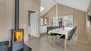 A modern interior with a wood-burning stove, a dining area with a table and chairs, and a kitchen visible through an open door. - VillaVilla 271 - Kegnæs, Sydjylland (Sydals)