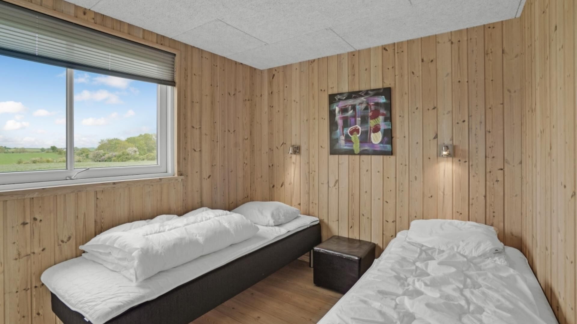 A bedroom with two beds, a window, and a painting on the wall.