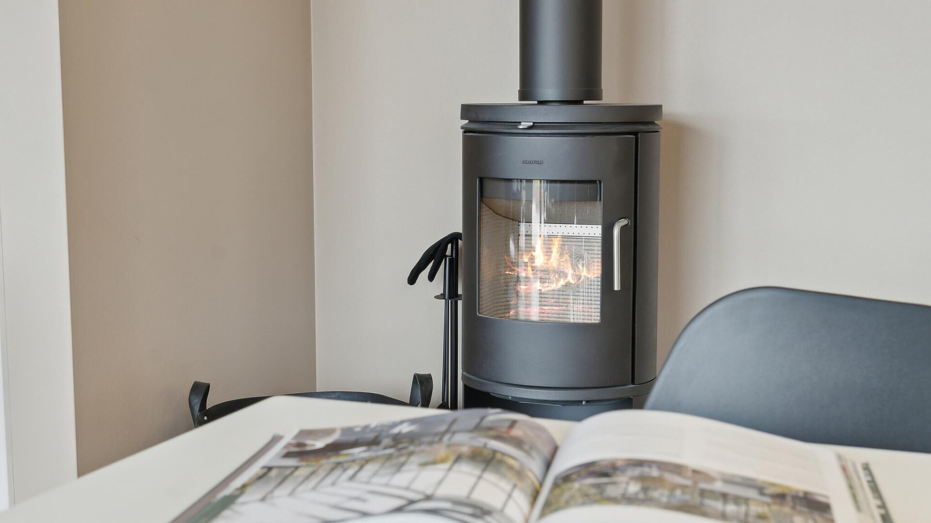 Ein moderner Holzofen mit Glastür, schwarzem Schornstein und einem Metallgriff.