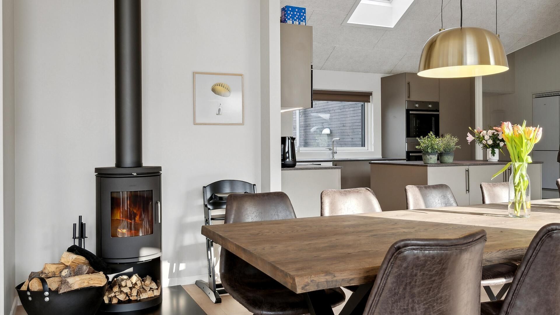 A modern kitchen with a central island, a dining area with a wooden table and leather chairs, and a wood-burning stove.