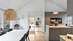 Une cuisine moderne dotée d’un grand îlot central, de luminaires suspendus et d’un coin repas avec une table et des chaises blanches.