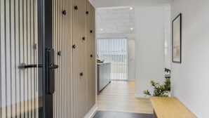 A modern interior with a kitchen area, a wooden door with black knobs, a white wall with a framed picture, and a small wooden table. - VillaVilla 683 - Blokhus, Nordjylland (Saltum)