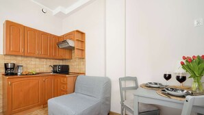 Una cucina compatta con mobili in legno, un divano grigio e un tavolo da pranzo per due, apparecchiato con piatti, bicchieri e un vaso di tulipani.