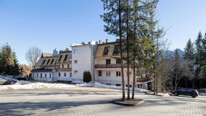 Un edificio residenziale con numerosi balconi, un'area di parcheggio pavimentata e vista su terreno innevato e montagne in lontananza.