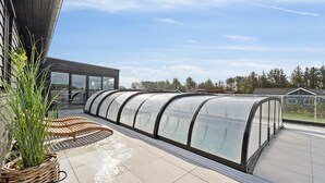 A modern building with a covered outdoor area featuring a curved glass enclosure, a wooden bench, and a potted plant. - VillaVilla 686 - Hostrup Strand, Limfjorden (Spøttrup)