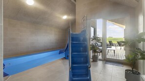A pool area with a blue slide, a covered patio with outdoor furniture, and a view of the countryside. - VillaVilla 906 - Skåstrup Strand, Fyn og øer (Bogense)