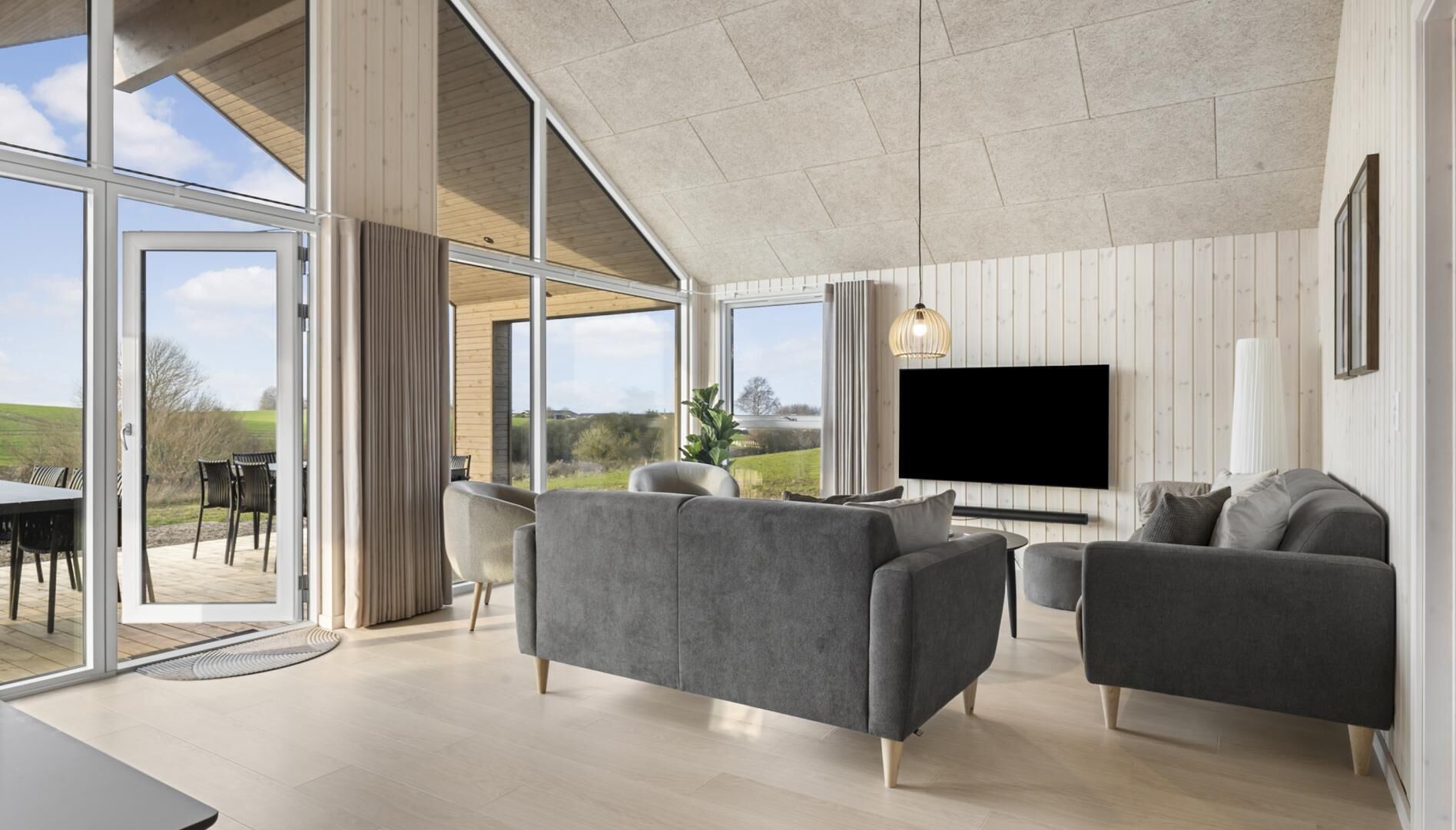 A spacious living room with a large TV, grey sofas, and a view of the outdoors.