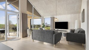 Un salon spacieux doté d’un grand téléviseur, de canapés gris et offrant une vue sur l’extérieur.