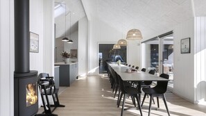 A modern kitchen with a built-in stove, a dining area with a long table and chairs, pendant lighting, and a view to the outside. - VillaVilla 907 - Skåstrup Strand, Fyn og øer (Bogense)