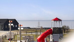A playground with a red slide, a small white and red structure, and a building with a black roof. - VillaVilla 907 - Skåstrup Strand, Fyn og øer (Bogense)