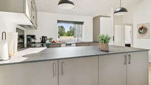Une cuisine moderne dotée d’un grand îlot central, d’appareils électroménagers intégrés et d’une fenêtre offrant une vue sur l’extérieur.