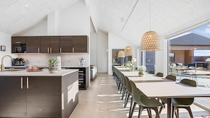 Eine moderne Küche mit dunklen Holzschränken, einer zentralen Kochinsel und einem Essbereich mit einem langen Tisch und Stühlen.