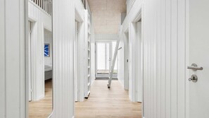 Ein Korridor mit weißen Türen, der zu einem Schlafzimmer mit einem Bett und einem blauen Kunstwerk führt.
