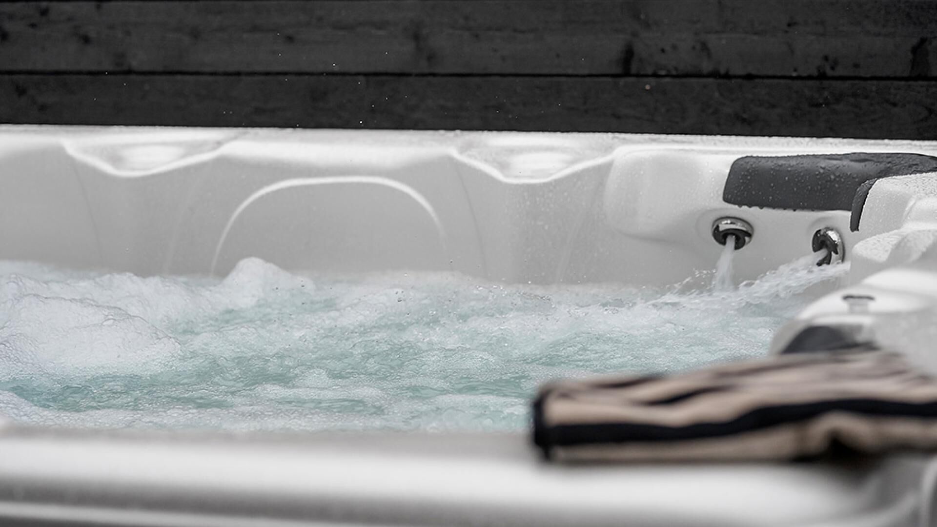 Un bain à remous avec jets d’eau, un banc en bois et un robinet en métal.