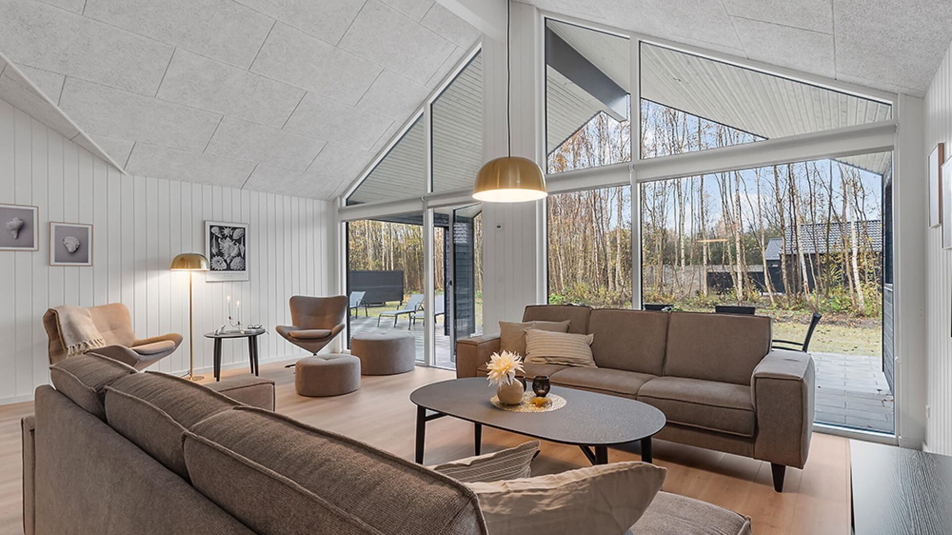 A spacious living room with a large sofa, a coffee table, and a chair. There are large windows providing a view of the outdoors.