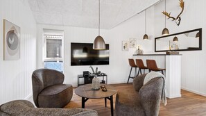 Ein modernes Wohnzimmer mit Fernseher, Sitzgelegenheiten und einem Essbereich mit Stühlen und Tisch.