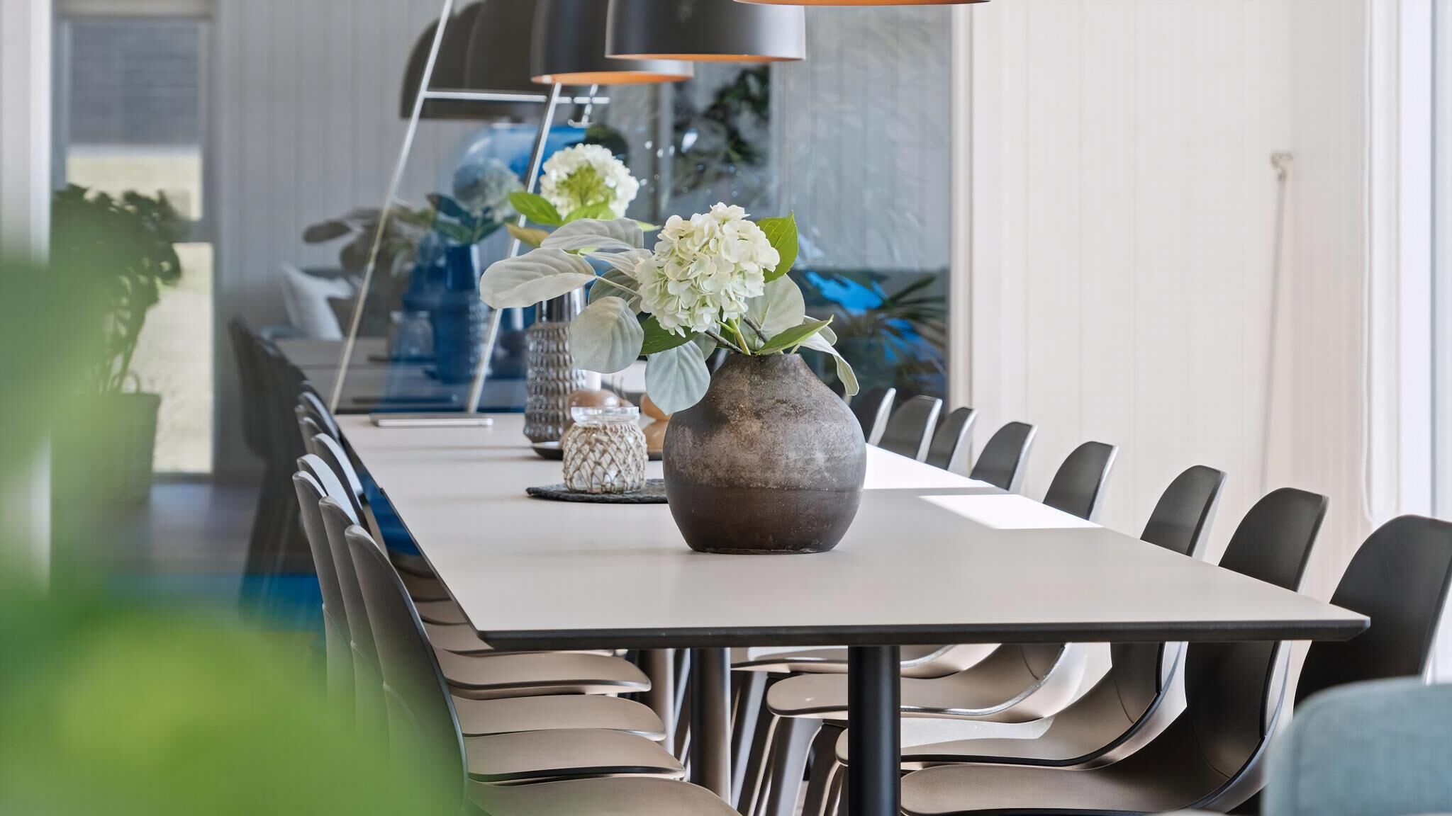 A modern dining area with a long table, chairs, and decorative vases.