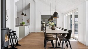 Eine moderne Küche mit Einbauherd, ein Essbereich mit großem Tisch und Stühlen sowie Pendelleuchten.