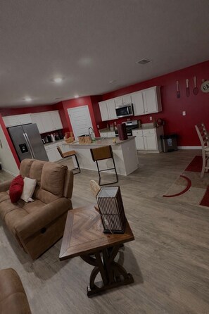 Una cocina moderna con armarios blancos, una isla central y un comedor con sofá marrón y una pequeña mesa de madera.