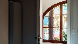 A room with a large arched window, a door, and a view of a palm tree outside. - Near the lake and the center (FLORIDA ASCONA Room 14) (Ascona)
