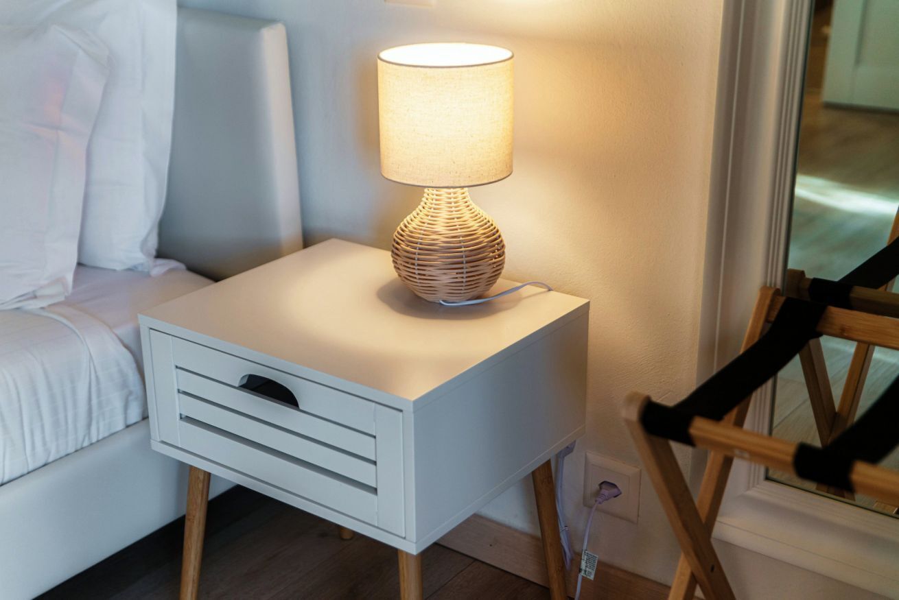 Une table de chevet avec une lampe, un tiroir et une chaise.