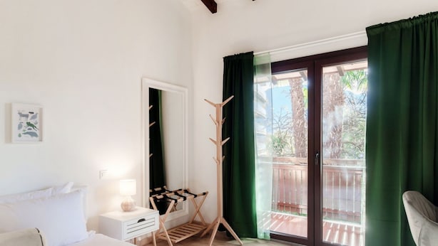 A bedroom with a bed, a bedside table with a lamp, a wooden drying rack, and a sliding glass door to an outdoor area. - Near the lake and the center (FLORIDA ASCONA Room 14) (Ascona)
