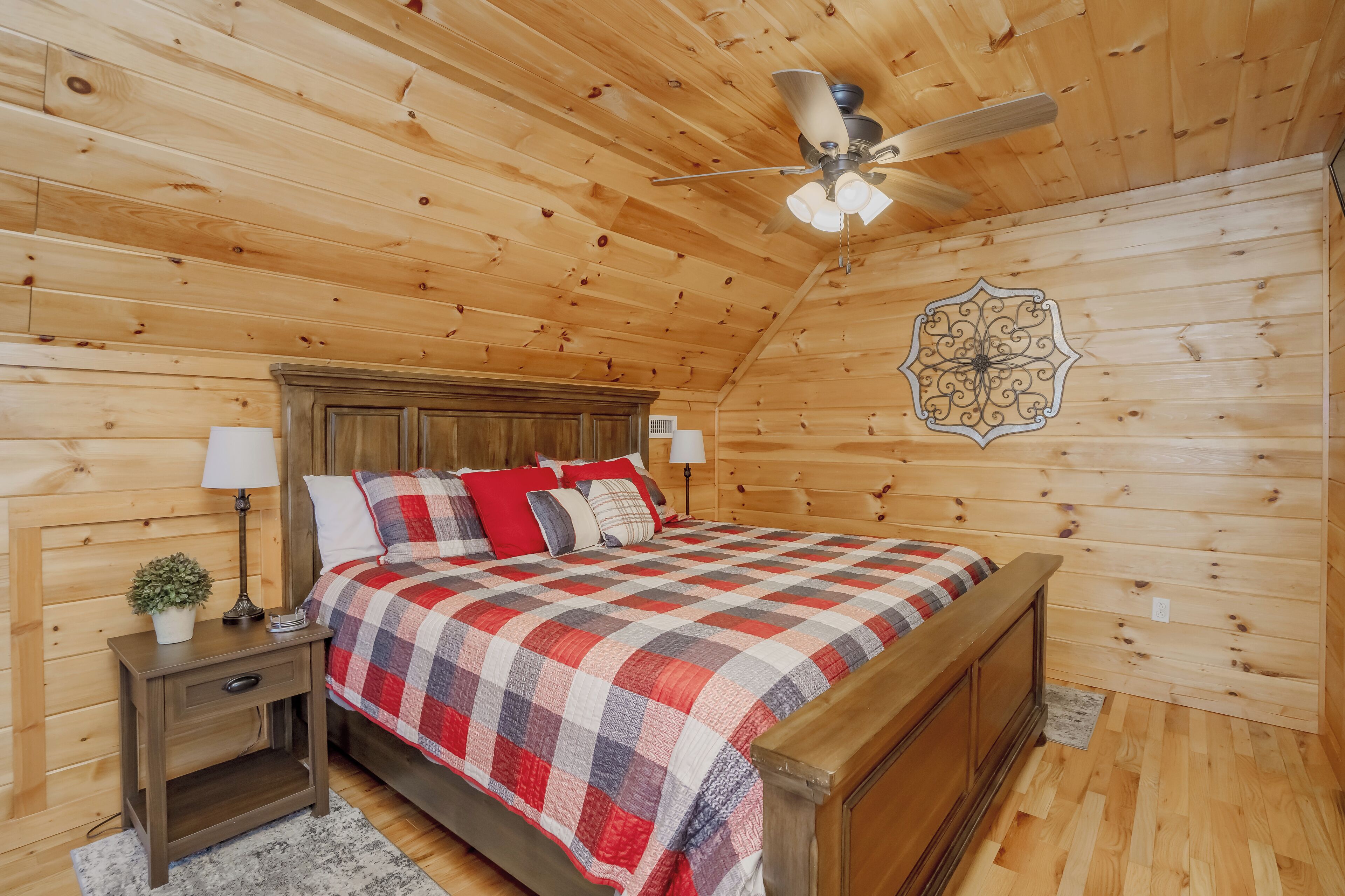 A wooden-paneled bedroom with a bed, nightstands, a ceiling fan, and a decorative wall piece.