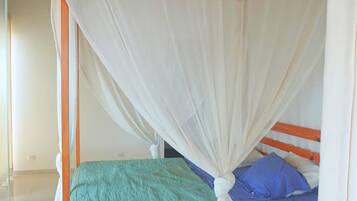 A single bed with a wooden frame, a green bedspread, and a blue pillow. A white canopy covers the bed.