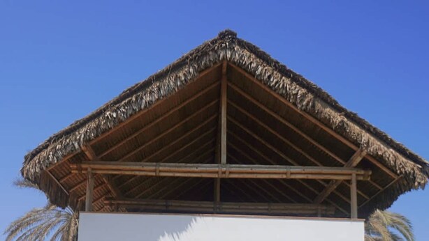 A modern building with a thatched roof, large windows, and a paved entrance area with benches and potted plants. - HOP Aloha Beachfront House With Direct Access (Chincha Baja)