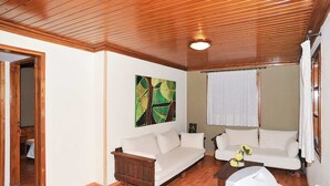 Ein Wohnzimmer mit Holzboden, Holzbalkendecke, einem weißen Sofa, einer Holzbank und einem Bild an der Wand.
