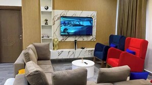 Un salon moderne avec un canapé d’angle, un téléviseur à écran plat et des fauteuils aux couleurs vives.