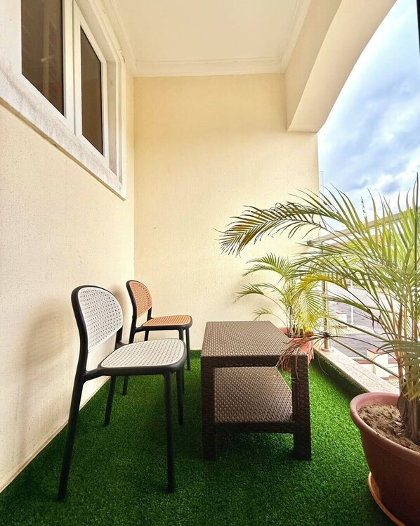 A balcony with artificial green turf, two wicker chairs, a small table, and a potted plant. - Declans Apartment (Abuja)