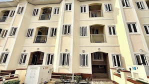 Un immeuble résidentiel à plusieurs étages, doté de balcons, de climatiseurs et d’un espace d’entrée pavé.