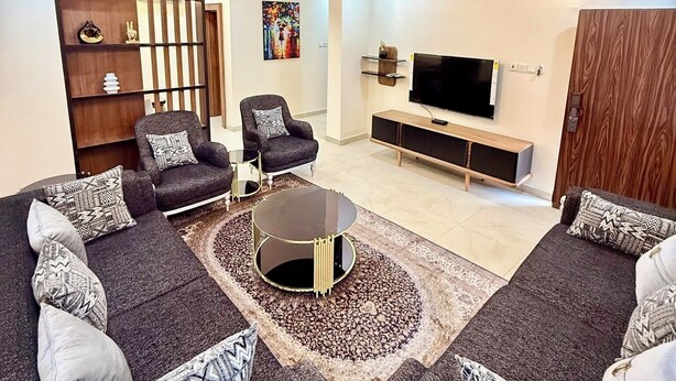 Un salon moderne comprenant un ensemble de canapés, une table basse, un téléviseur et un élément de séparation décoratif.