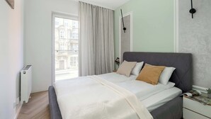 A bedroom with a bed, a radiator, a window with curtains, and a wall clock. - Spacious Apartment | 2 Bedrooms | Underground Parking (Poznań)