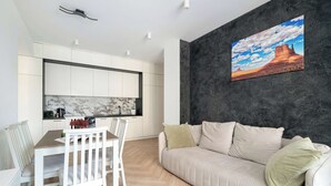 A modern living room with a sofa, a dining table with chairs, and a kitchen area with white cabinets and a marble backsplash. - Spacious Apartment | 2 Bedrooms | Underground Parking (Poznań)